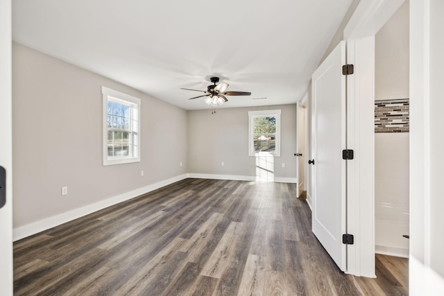 interior space featuring a healthy amount of sunlight, dark wood-style floors, baseboards, and a ceiling fan