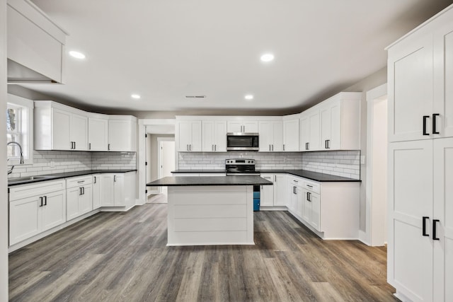 kitchen featuring dark wood finished floors, white cabinets, dark countertops, appliances with stainless steel finishes, and a sink