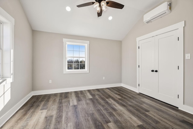 unfurnished bedroom featuring a wall unit AC, baseboards, dark wood finished floors, and lofted ceiling