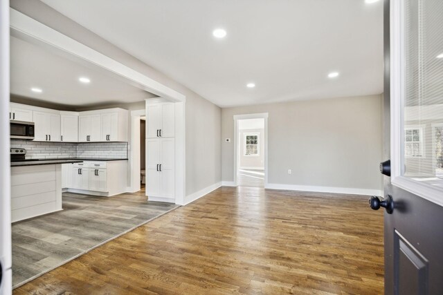 kitchen featuring tasteful backsplash, dark countertops, stainless steel microwave, white cabinetry, and wood finished floors