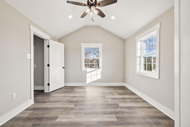 interior space with a ceiling fan, vaulted ceiling, baseboards, and wood finished floors