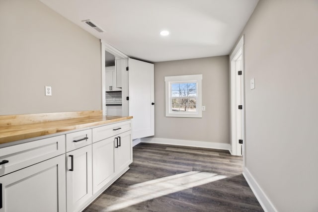 kitchen featuring baseboards, visible vents, butcher block counters, dark wood-type flooring, and white cabinetry