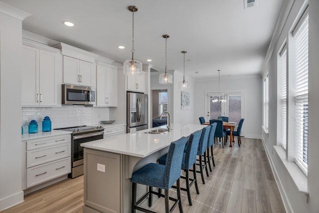 kitchen featuring stainless steel appliances, light countertops, pendant lighting, and a kitchen island with sink