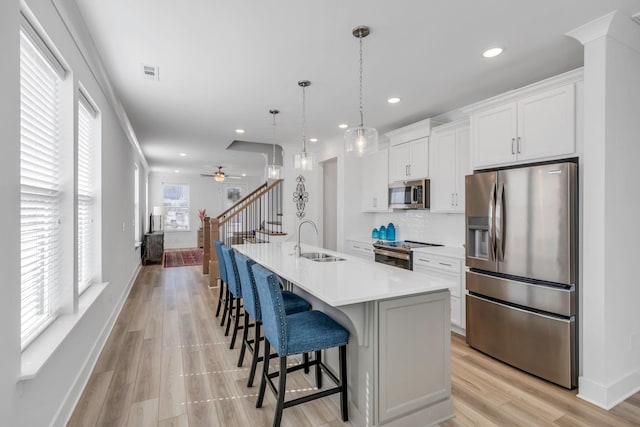 kitchen with stainless steel appliances, a sink, light countertops, a center island with sink, and pendant lighting