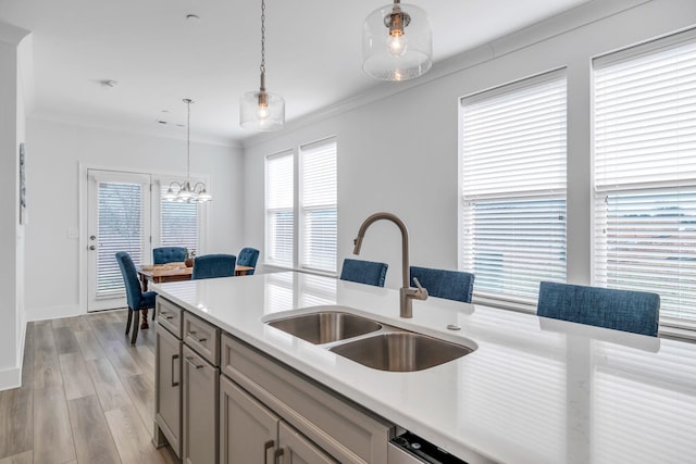 kitchen with crown molding, light countertops, a sink, and pendant lighting