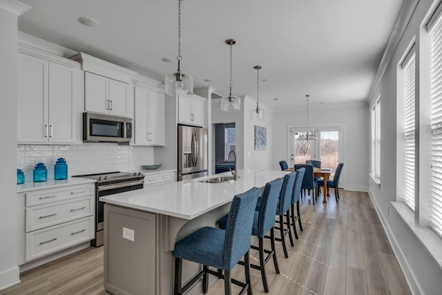 kitchen featuring an island with sink, appliances with stainless steel finishes, light countertops, and a sink