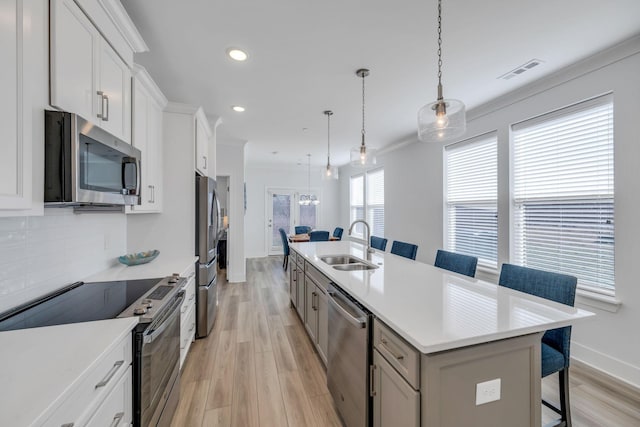 kitchen with a breakfast bar, decorative light fixtures, a kitchen island with sink, stainless steel appliances, and light countertops