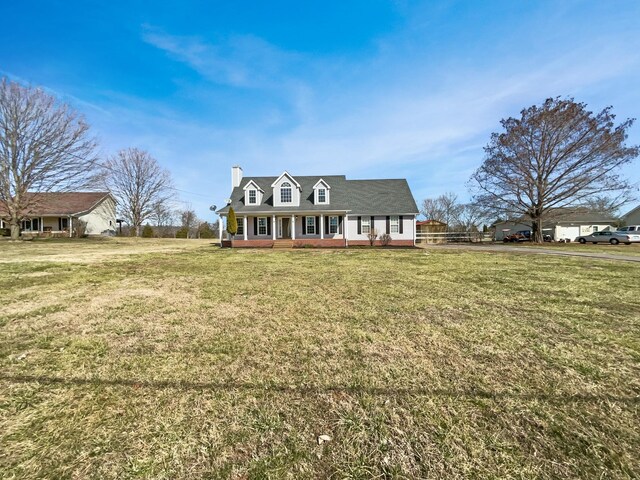 cape cod house with a front yard, covered porch, and a chimney