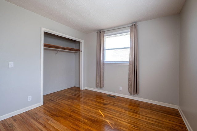 unfurnished bedroom featuring a textured ceiling, wood finished floors, visible vents, and baseboards