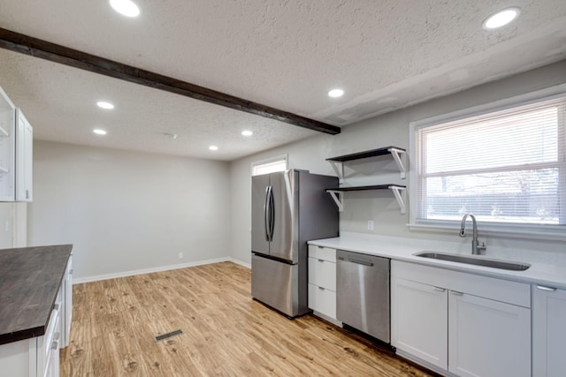 kitchen with light wood finished floors, butcher block counters, appliances with stainless steel finishes, white cabinets, and a sink