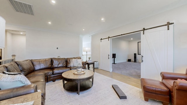 living room with a barn door, visible vents, light wood-style flooring, ornamental molding, and recessed lighting