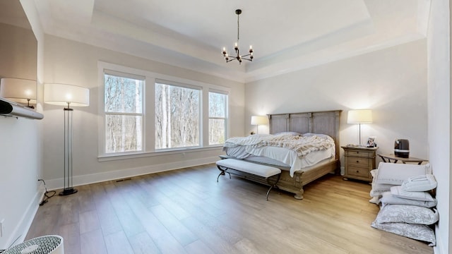 bedroom with a notable chandelier, a tray ceiling, wood finished floors, and baseboards