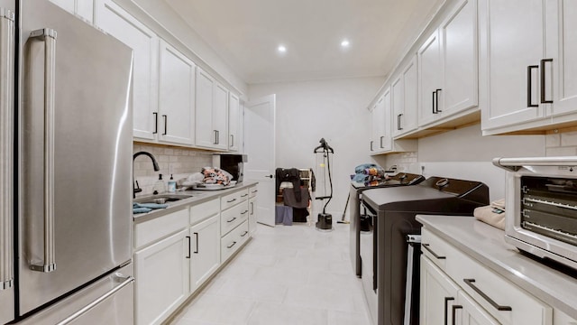 kitchen featuring high end refrigerator, a sink, white cabinets, washer and dryer, and light countertops