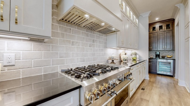 kitchen with range with two ovens, light wood-style flooring, beverage cooler, custom exhaust hood, and decorative backsplash