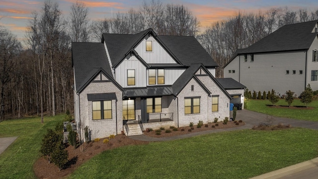 modern farmhouse style home with brick siding, driveway, a lawn, board and batten siding, and a standing seam roof