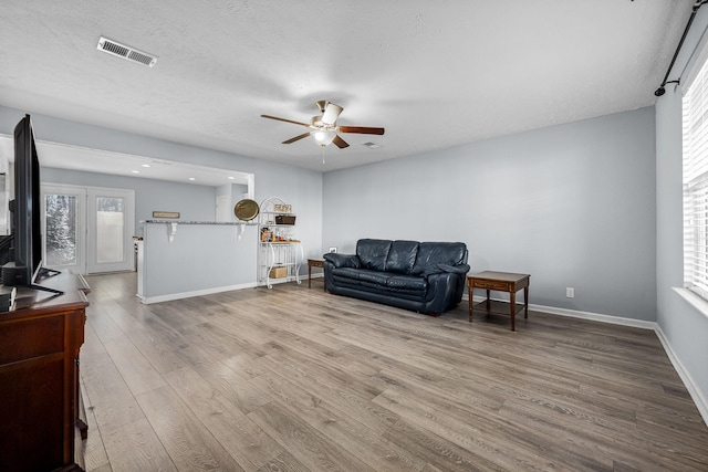 living room featuring a ceiling fan, visible vents, baseboards, light wood finished floors, and plenty of natural light