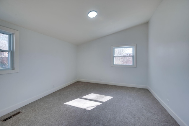 carpeted empty room with vaulted ceiling, visible vents, and baseboards