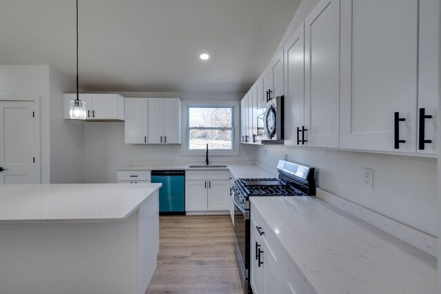 kitchen featuring light wood finished floors, appliances with stainless steel finishes, decorative light fixtures, white cabinetry, and a sink