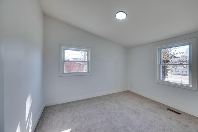 spare room featuring baseboards, visible vents, vaulted ceiling, and light colored carpet