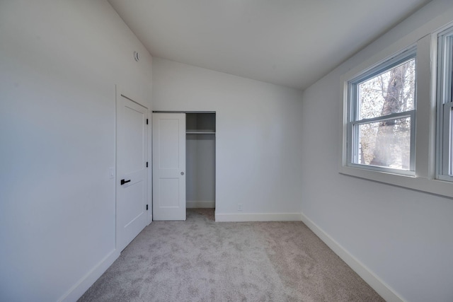 unfurnished bedroom featuring vaulted ceiling, a closet, baseboards, and light colored carpet