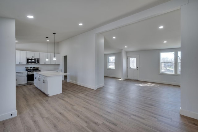 kitchen featuring appliances with stainless steel finishes, open floor plan, decorative light fixtures, light countertops, and white cabinetry