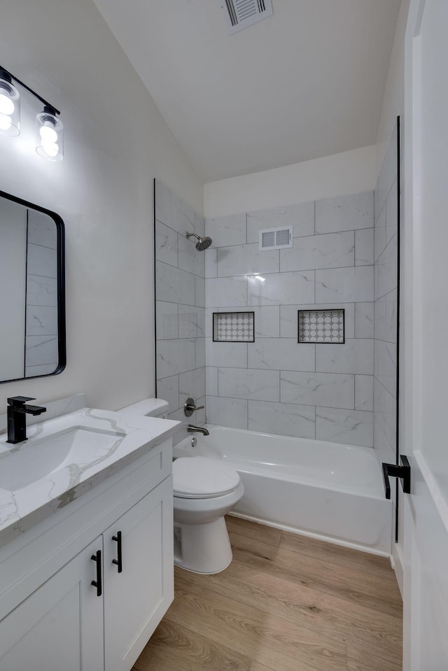 full bathroom with visible vents, toilet, wood finished floors, vanity, and washtub / shower combination