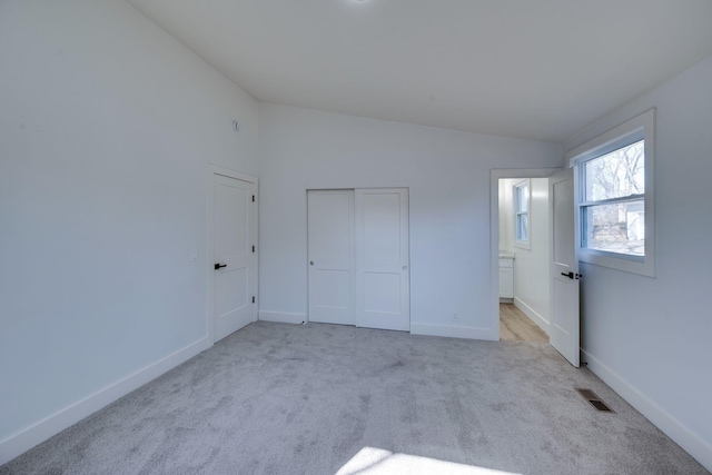 unfurnished bedroom with light carpet, visible vents, baseboards, lofted ceiling, and ensuite bathroom