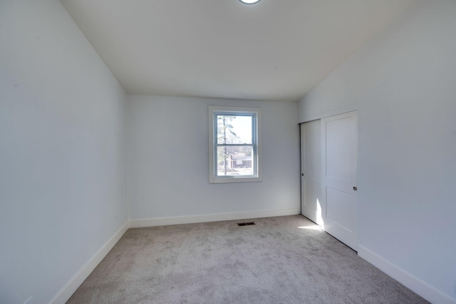 unfurnished room with lofted ceiling, light carpet, visible vents, and baseboards