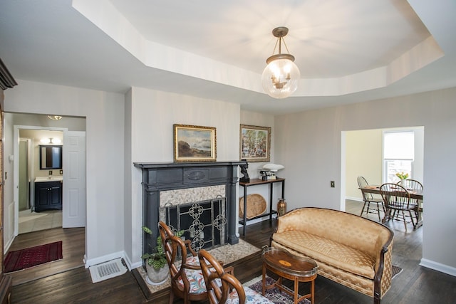 living room featuring dark wood-style floors, a fireplace with flush hearth, a raised ceiling, and visible vents