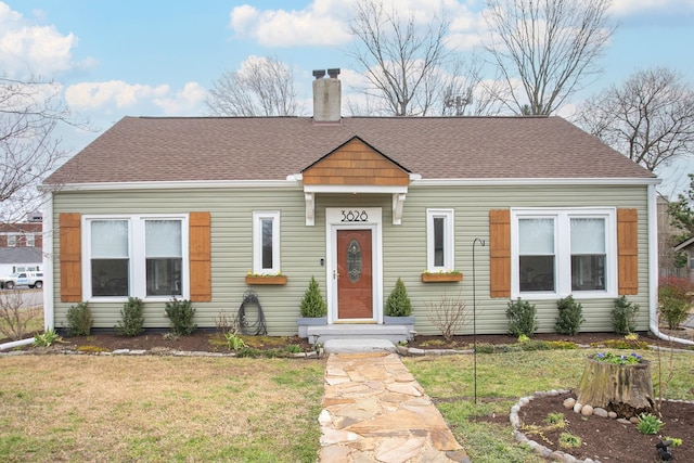 view of front of property featuring a chimney, roof with shingles, and a front yard