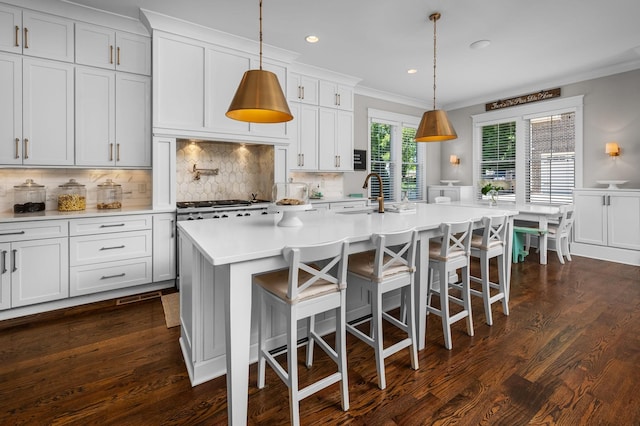 kitchen featuring light countertops, a center island with sink, white cabinetry, and decorative light fixtures