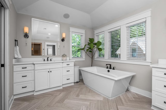 bathroom featuring a freestanding tub, baseboards, vaulted ceiling, and vanity