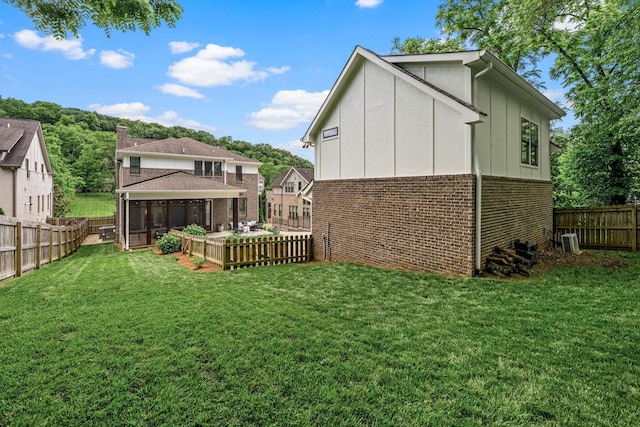 rear view of house featuring a sunroom, brick siding, a lawn, and a fenced backyard