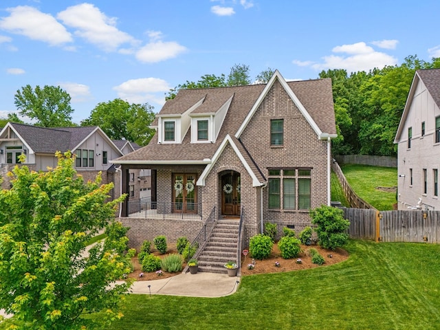 tudor house featuring brick siding, a shingled roof, a front yard, crawl space, and fence