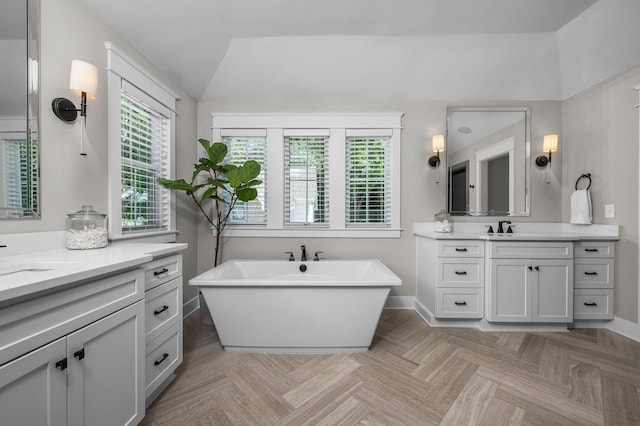 full bath with lofted ceiling, two vanities, a sink, baseboards, and a soaking tub