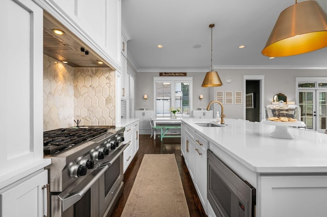 kitchen with appliances with stainless steel finishes, white cabinets, a center island with sink, and hanging light fixtures