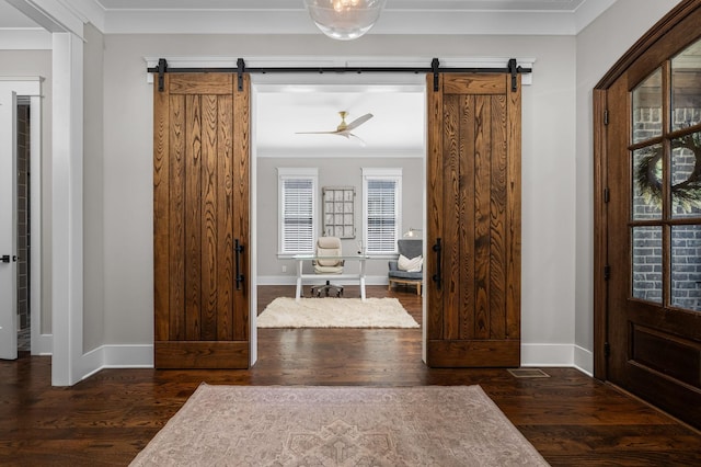 foyer featuring ornamental molding, a barn door, dark wood-style flooring, and baseboards