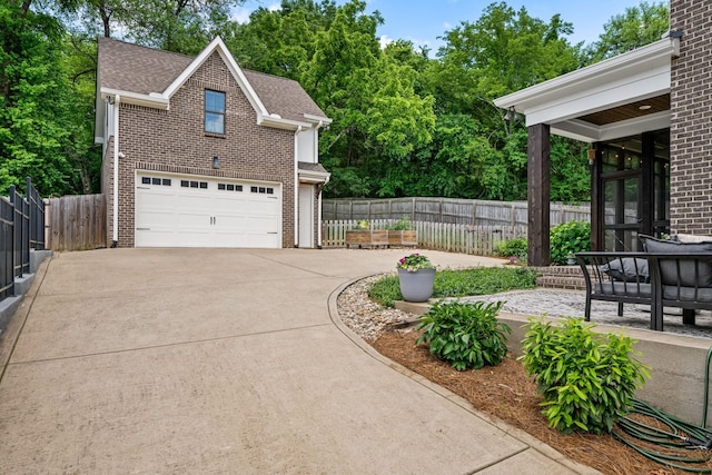 view of side of home with concrete driveway, brick siding, an attached garage, and roof with shingles