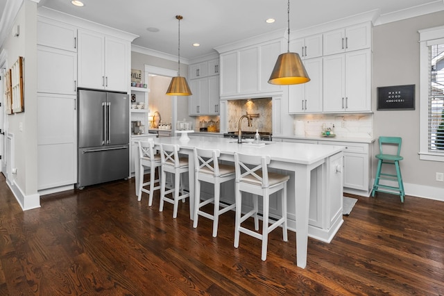 kitchen featuring high quality fridge, a sink, white cabinetry, light countertops, and pendant lighting