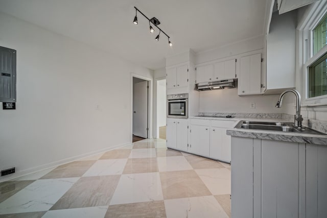 kitchen featuring oven, under cabinet range hood, a sink, white cabinetry, and light countertops