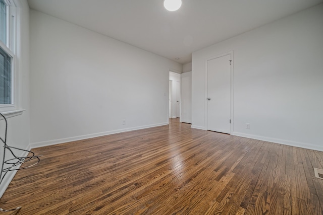 unfurnished room with dark wood-style flooring, visible vents, and baseboards