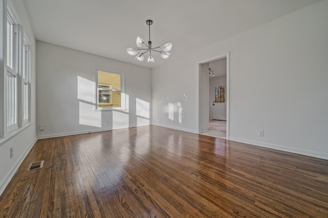 spare room featuring a chandelier, visible vents, baseboards, and hardwood / wood-style flooring