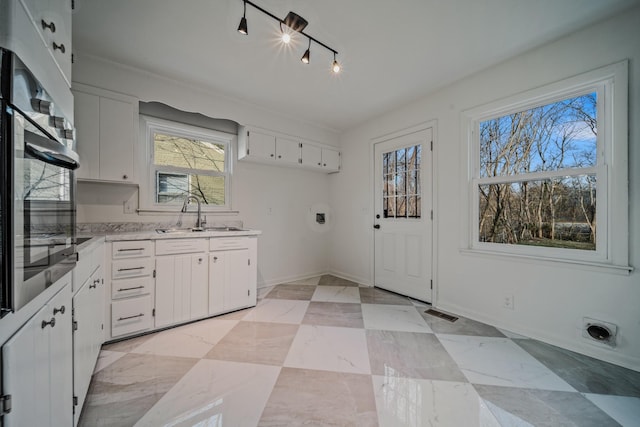 interior space with baseboards, oven, light countertops, white cabinetry, and a sink