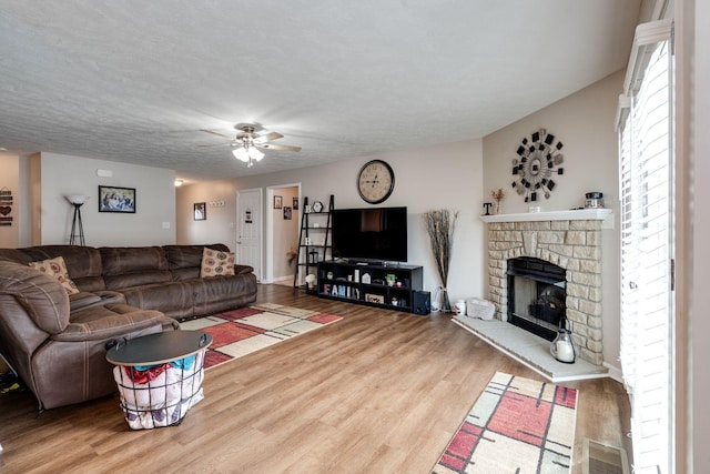 living area with ceiling fan, a fireplace, visible vents, and wood finished floors