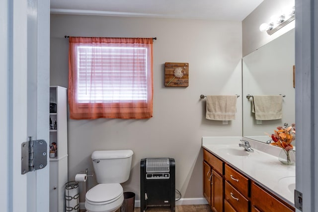 bathroom featuring heating unit, double vanity, toilet, a sink, and baseboards