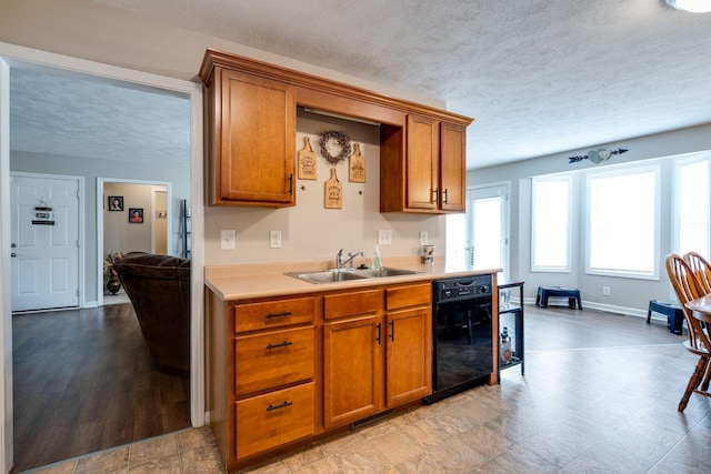 kitchen featuring brown cabinetry, black dishwasher, light countertops, and a sink