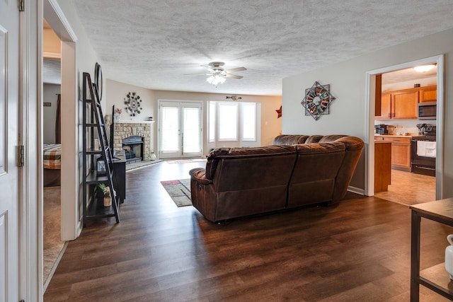 living area featuring dark wood-type flooring, a fireplace, a textured ceiling, and ceiling fan