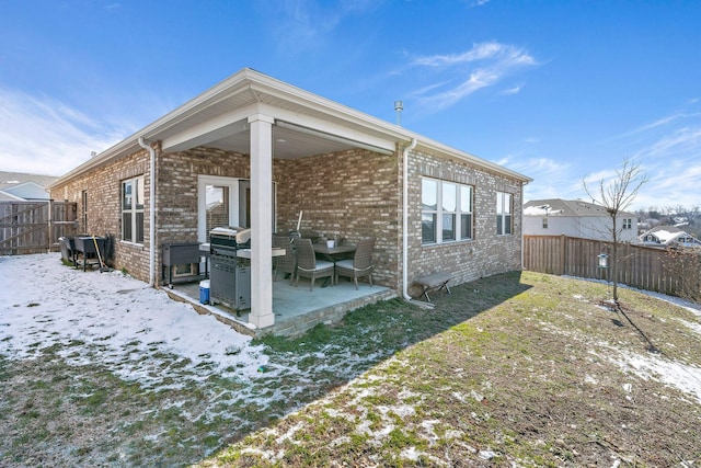 snow covered rear of property with brick siding, a patio area, and fence