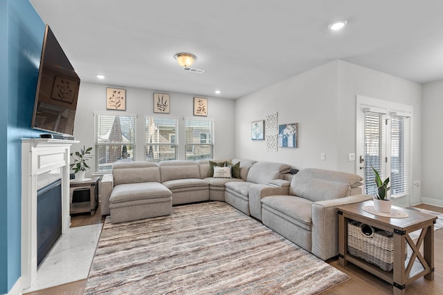 living area featuring light wood-style floors, recessed lighting, visible vents, and a high end fireplace