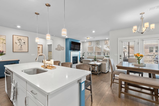 kitchen featuring decorative light fixtures, a sink, a center island with sink, and white cabinets